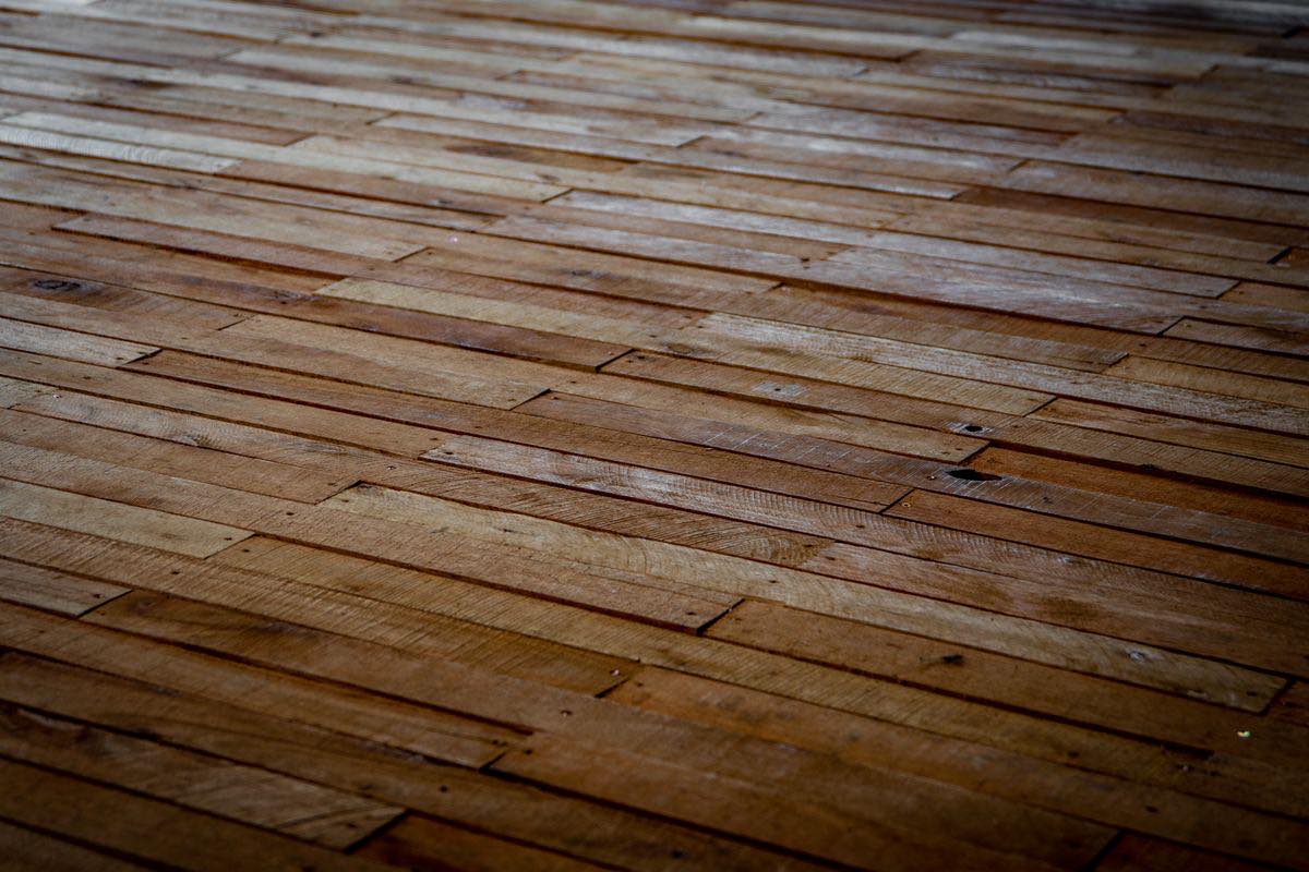 A close view of a timber floor from a low angle, with narrow boards of different lengths laid side by side and nail holes visible along the joints.